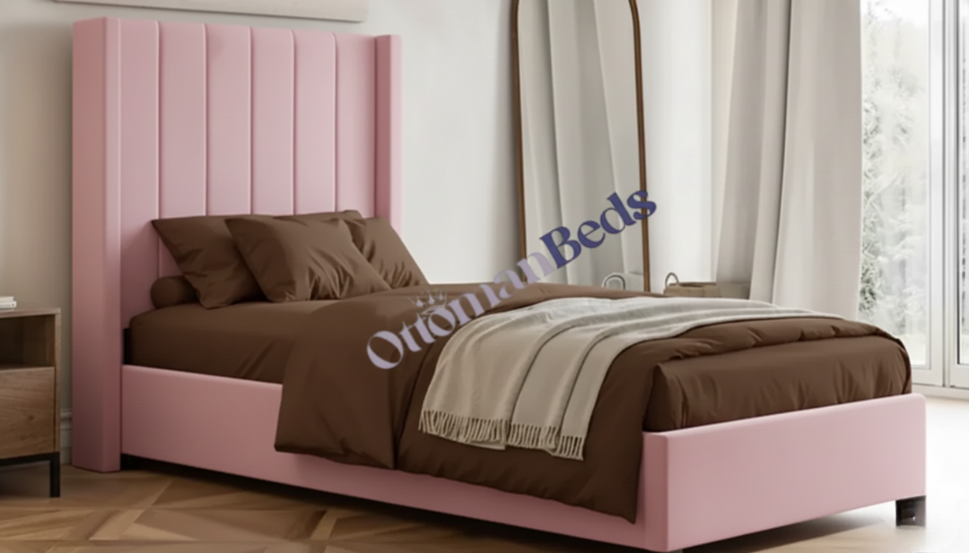 A pink single ottoman bed with a modern design, featuring a tufted headboard and brown bedding, in a bright room with natural light and a full-length mirror.