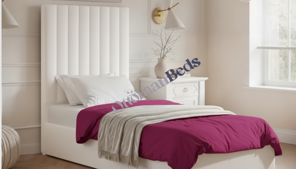 Single Ottomans bed with a tall white panelled headboard, white pillows, magenta bedding, and a soft beige throw in a bright, cozy bedroom with a nightstand and window.